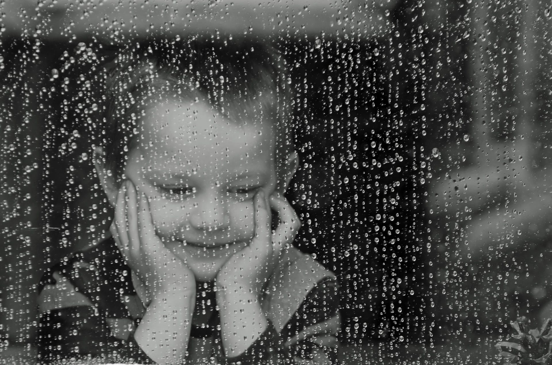 A child looks longingly out of a window at the rain outside their house.